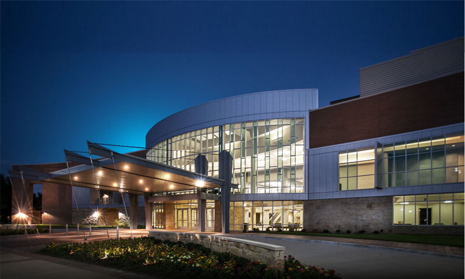 A modern building with a glass facade and a large entrance canopy at night in McLennan County, Texas.