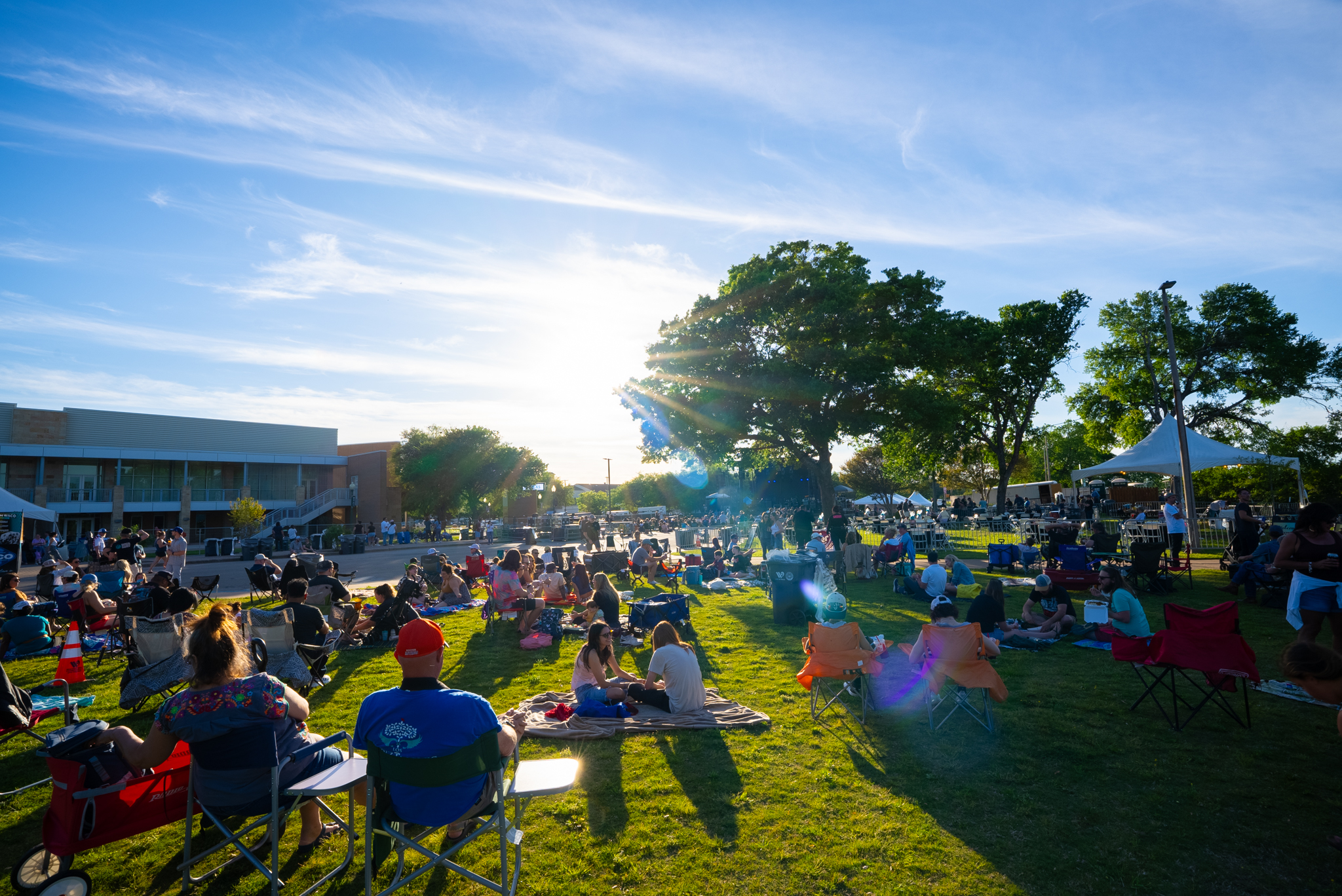 People sitting on a grassy lawn at an outdoor event during a sunny day in McLennan County, Texas.