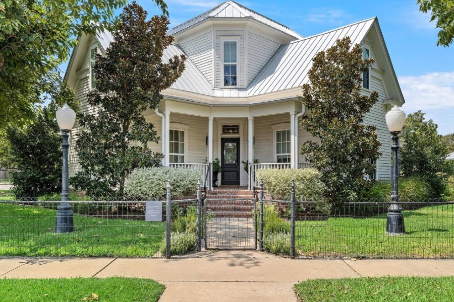 A charming white house with a metal roof and a fenced front yard in McLennan County, Texas.