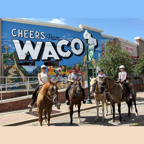 Four people on horseback posing in front of a Cheers from Waco mural in McLennan County, Texas.