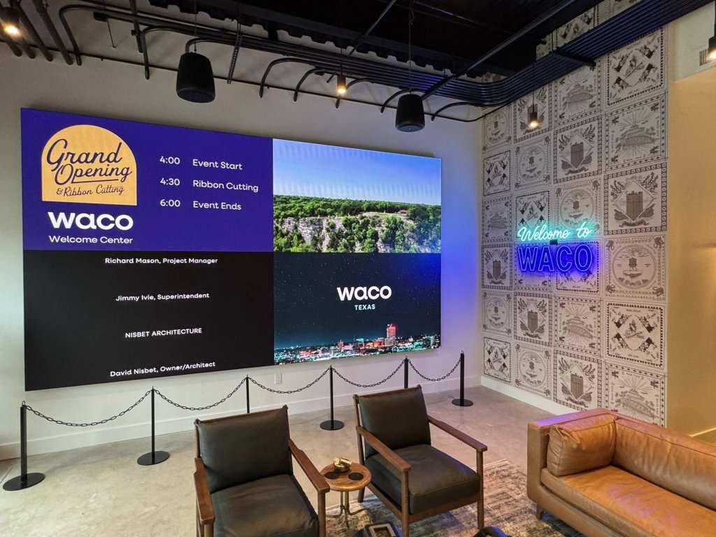 A modern lobby with a large digital display showing a Waco welcome center event schedule in McLennan County, Texas.