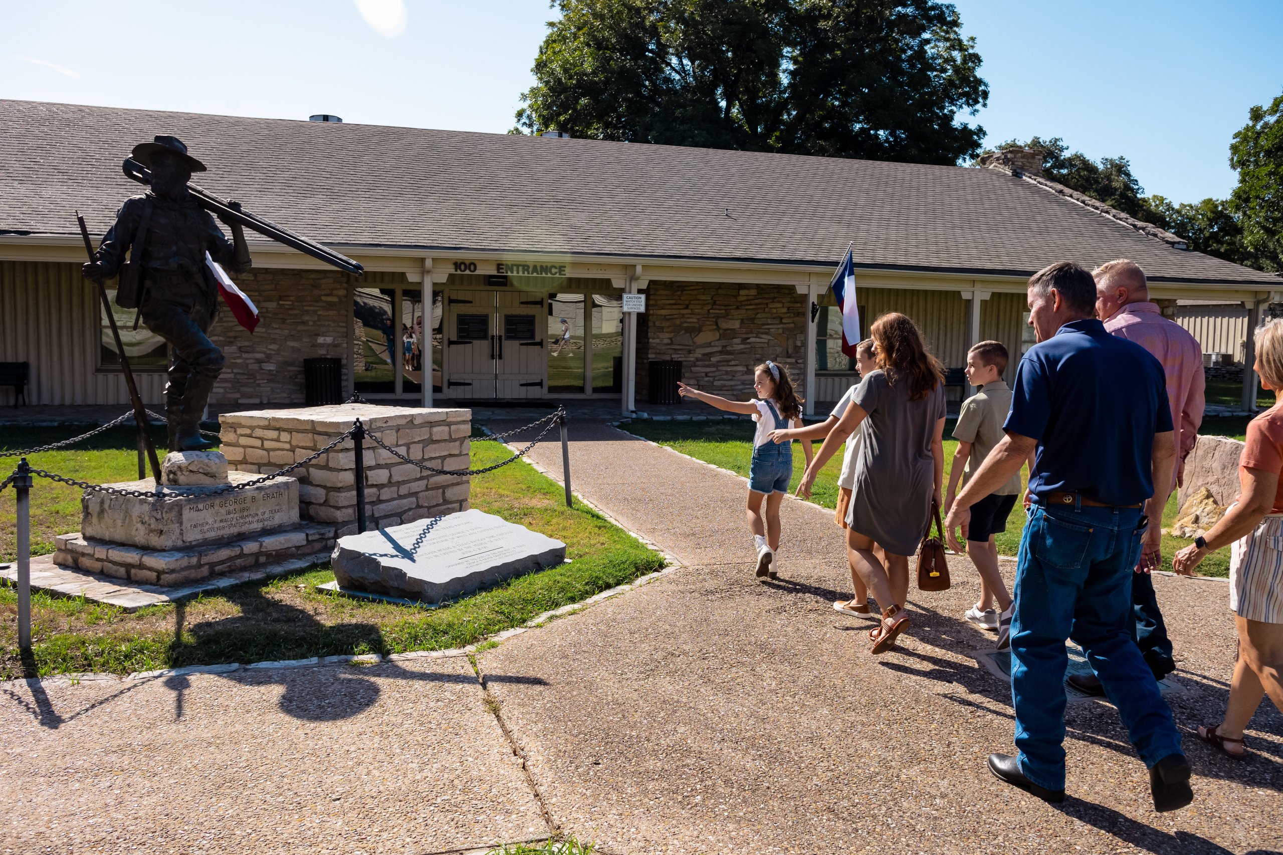 A family walks toward a building entrance past a bronze statue of a soldier in McLennan County, Texas.