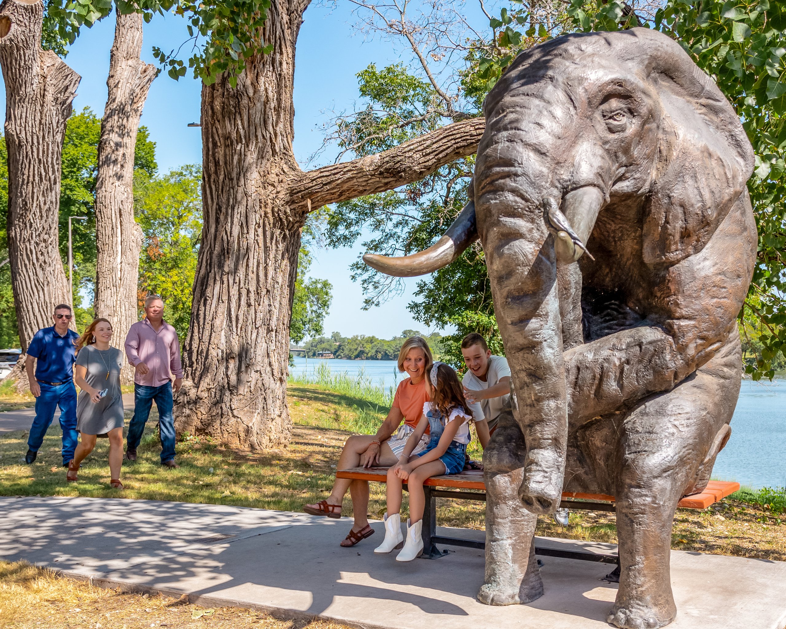 A family poses for a photo next to a large bronze elephant statue outdoors in McLennan County, Texas.