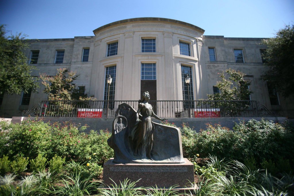 A bronze statue of a woman stands before a large, classical-style stone building in McLennan County, Texas.