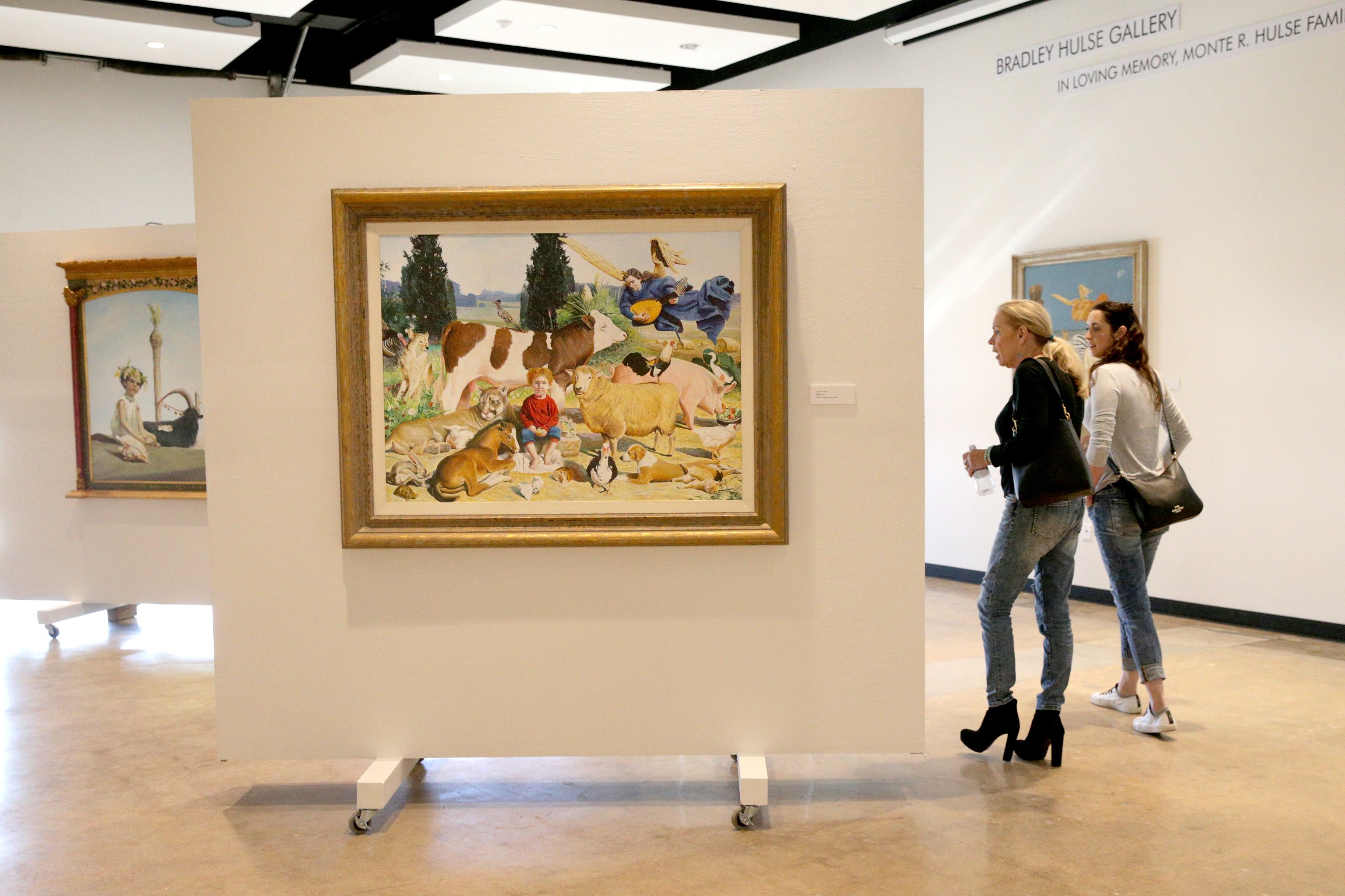Two women view a large painting of animals and a child in an art gallery in McLennan County, Texas.