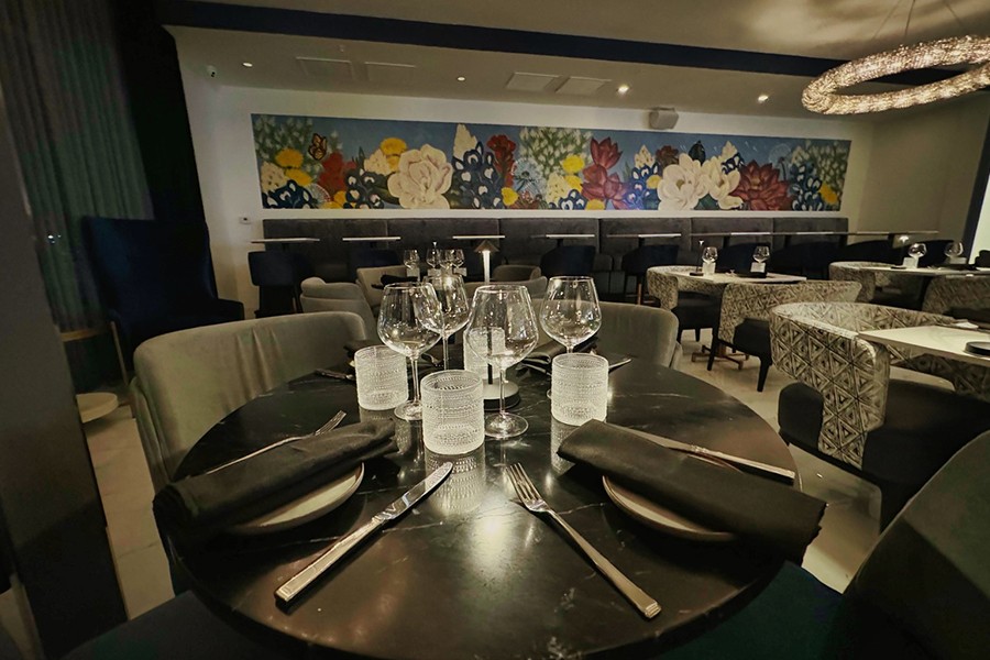 A dimly lit, elegant restaurant interior with a floral mural and set dining tables in McLennan County, Texas.