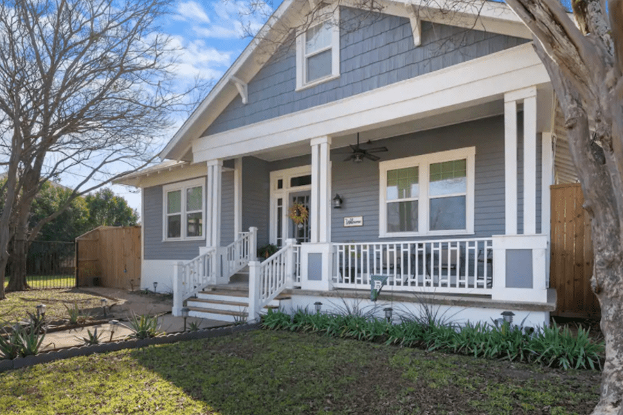 A charming blue house with a white porch and front yard in McLennan County, Texas.