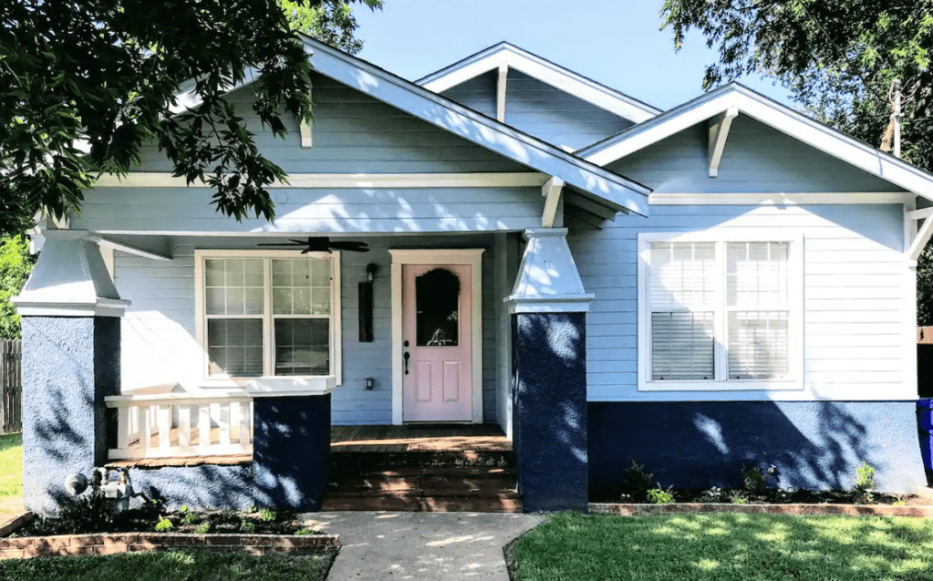 A light blue house with a dark blue base and a pink front door in McLennan County, Texas.