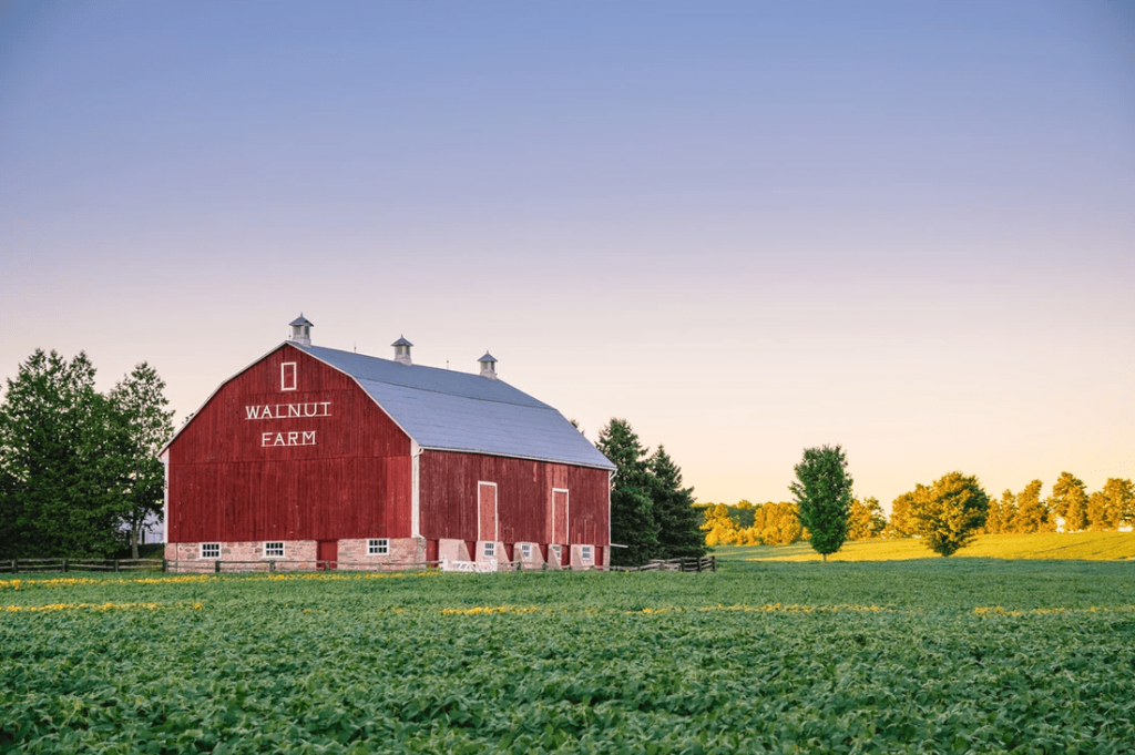 A red barn labeled Walnut Farm stands in a green field at sunset in McLennan County, Texas.