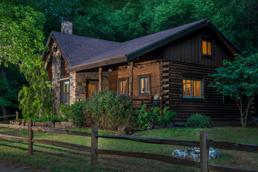 A rustic log cabin with stone accents sits nestled in a lush green forest in McLennan County, Texas.