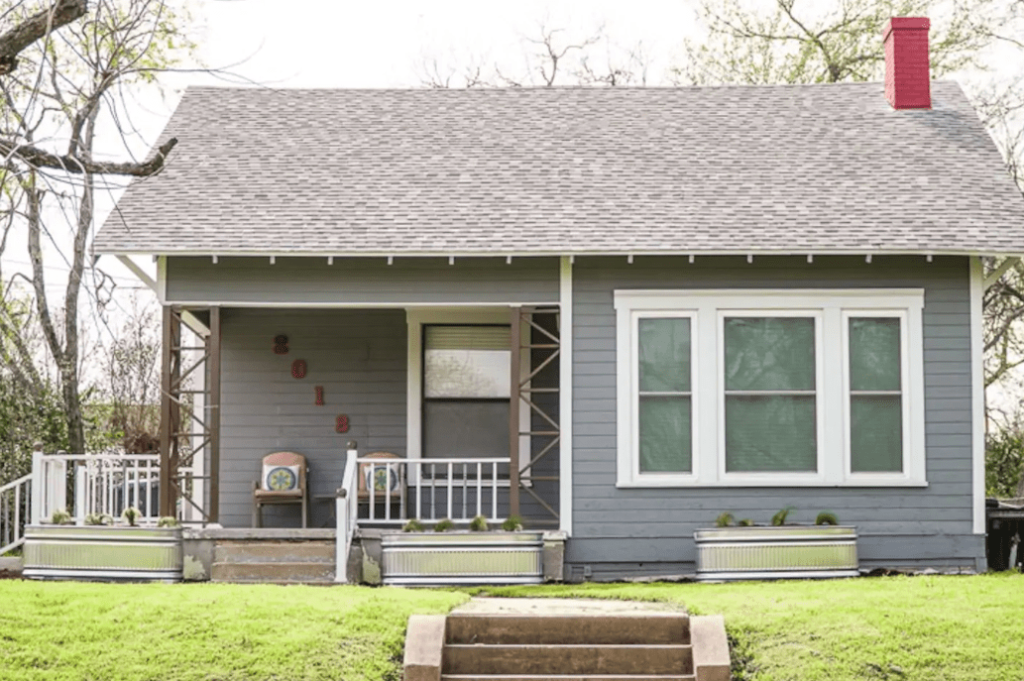 A grey cottage with a red chimney and a front porch with metal planters in McLennan County, Texas.