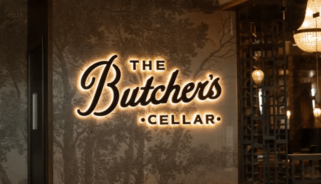 An illuminated sign for The Butcher's Cellar on a decorative wall in McLennan County, Texas.