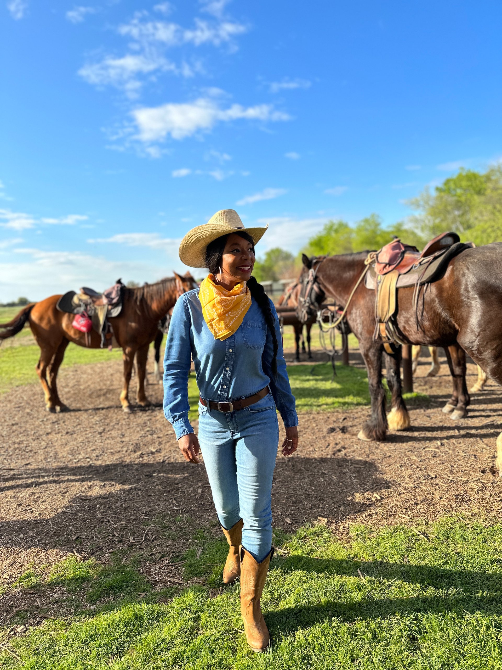 A woman in a cowboy hat and denim outfit stands near horses in a field in McLennan County, Texas.
