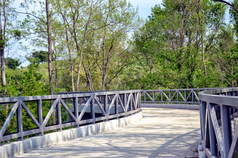 A curved concrete walkway with grey railings winds through a lush green forest in McLennan County, Texas.