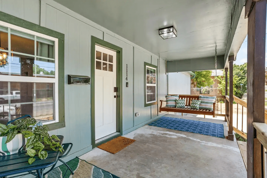 A covered front porch with a hanging swing, blue rug, and a small table in McLennan County, Texas.