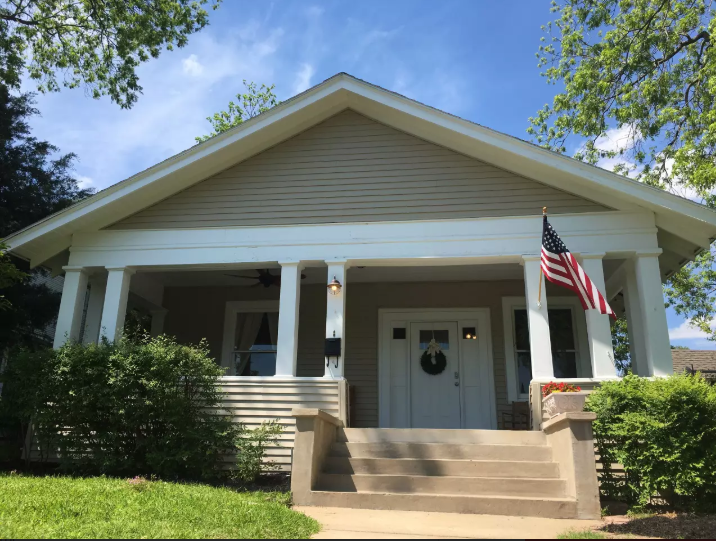 A charming bungalow house with a front porch and an American flag in McLennan County, Texas.