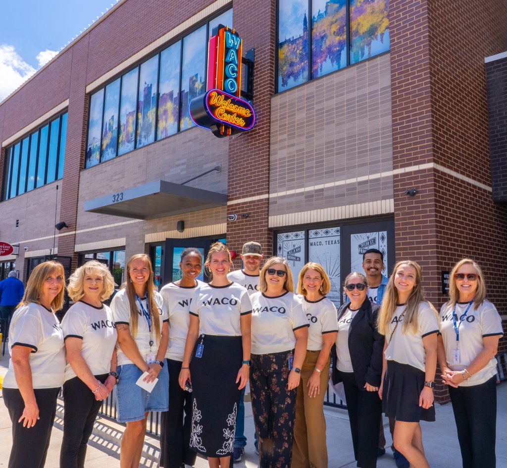 A group of people wearing Waco t-shirts standing in front of the Waco Welcome Center in McLennan County, Texas.