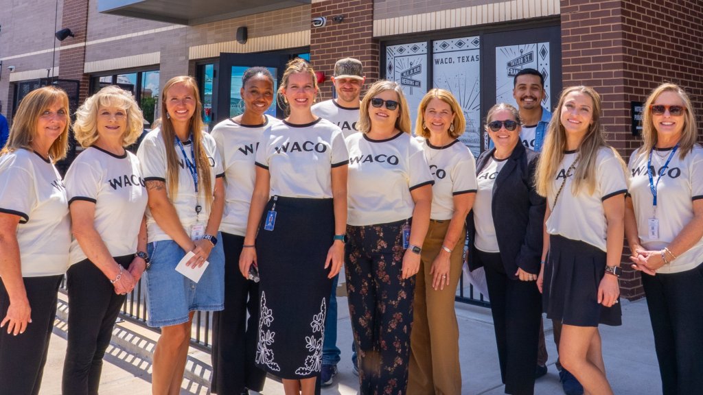 A group of people wearing matching Waco t-shirts standing outside a brick building in McLennan County, Texas.