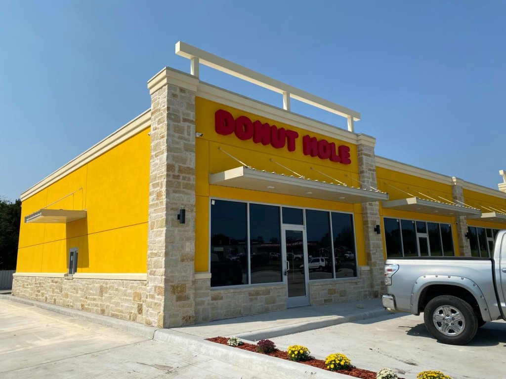 A bright yellow Donut Hole shop exterior with stone accents under a clear blue sky in McLennan County, Texas.