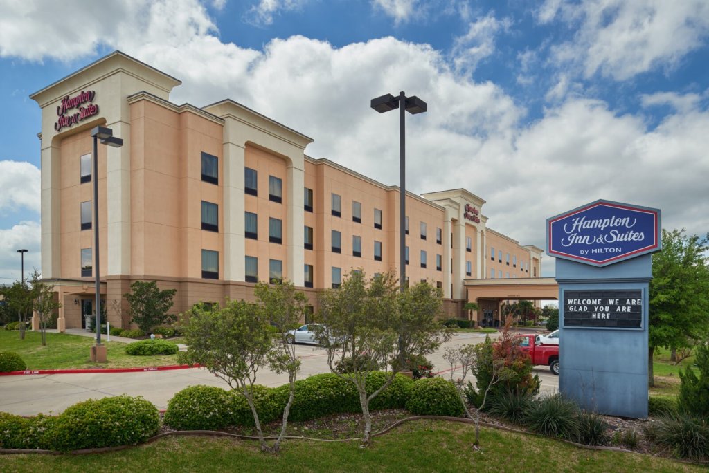 A Hampton Inn and Suites hotel building with a welcome sign under a cloudy sky in McLennan County, Texas.
