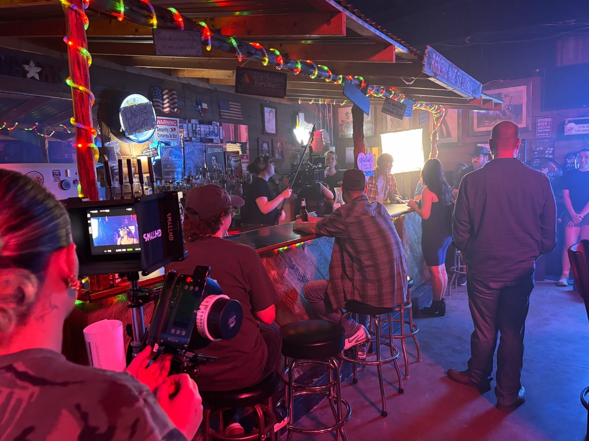 A film crew records a scene inside a dimly lit bar with colorful lights in McLennan County, Texas.
