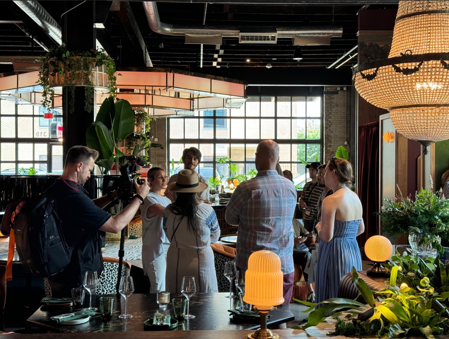 A film crew records a group of people gathered in a stylish, well-lit restaurant in McLennan County, Texas.