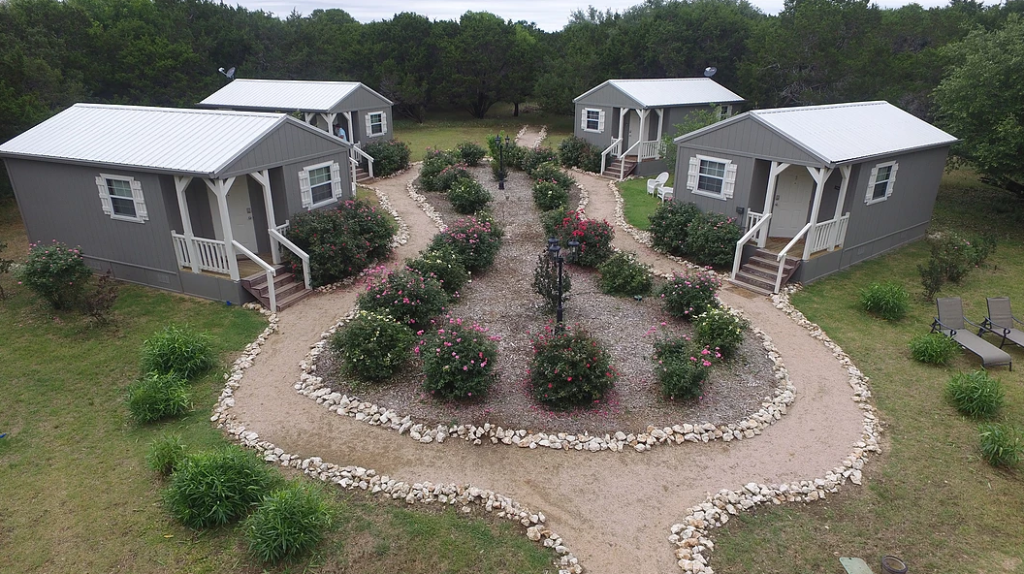 Three small grey cabins arranged around a central garden with rose bushes and paths in McLennan County, Texas.