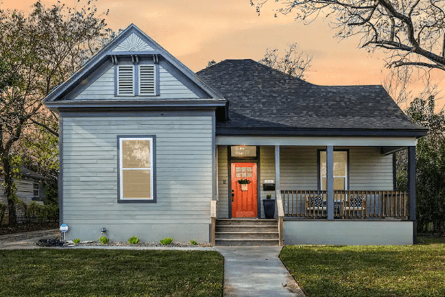 A charming light blue house with a vibrant orange front door and a front porch in McLennan County, Texas.