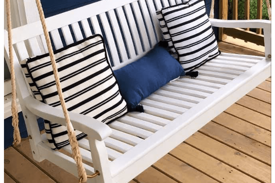 A white wooden porch swing with striped and blue pillows on a wooden deck in McLennan County, Texas.