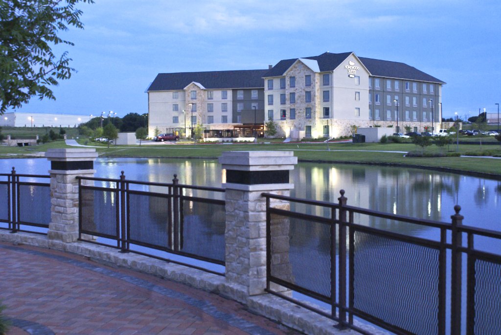 A Homewood Suites hotel building viewed across a calm pond at dusk in McLennan County, Texas.