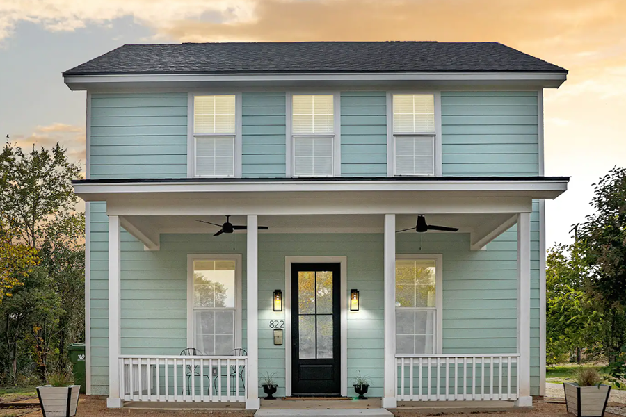 A two-story light blue house with a front porch and black door in McLennan County, Texas.