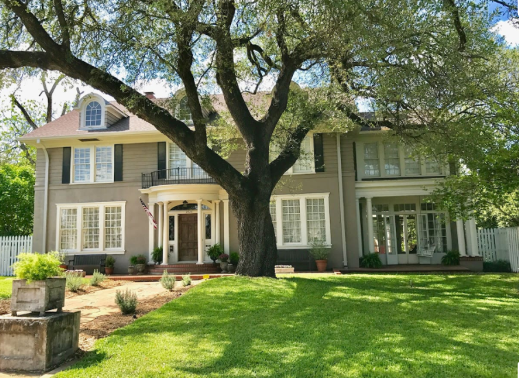 A large, two-story colonial-style house with a prominent oak tree in the front yard in McLennan County, Texas.