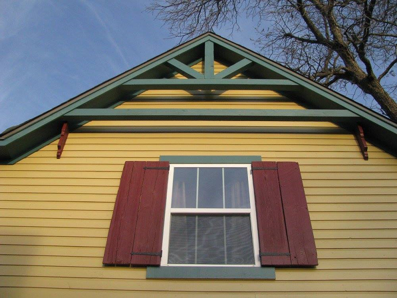 A low-angle view of a yellow house gable with a window and red shutters in McLennan County, Texas.