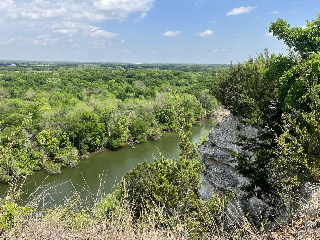 A river winds through a lush green forest viewed from a rocky cliff in McLennan County, Texas.