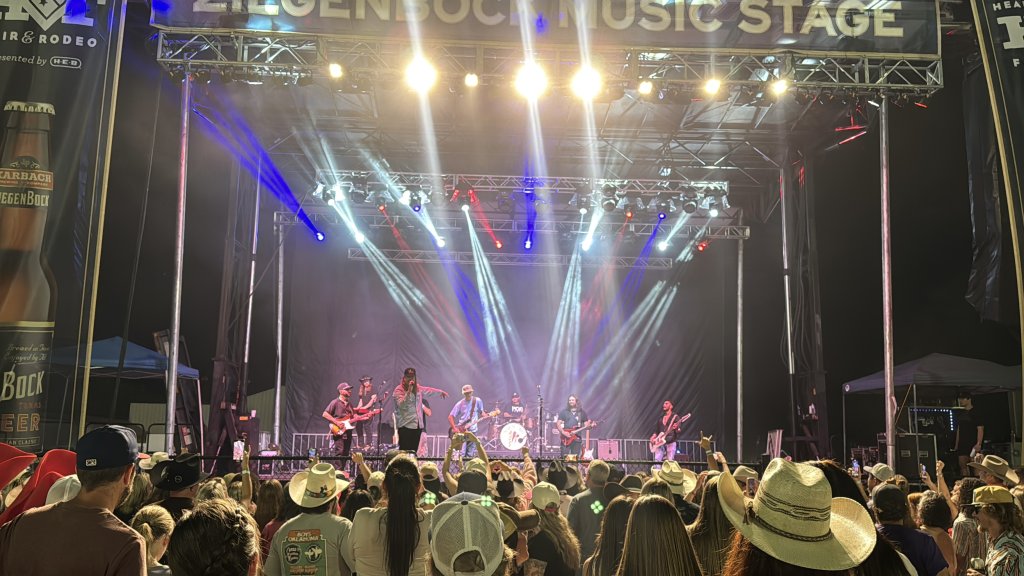 A band performs on a brightly lit outdoor music stage before a large crowd in McLennan County, Texas.