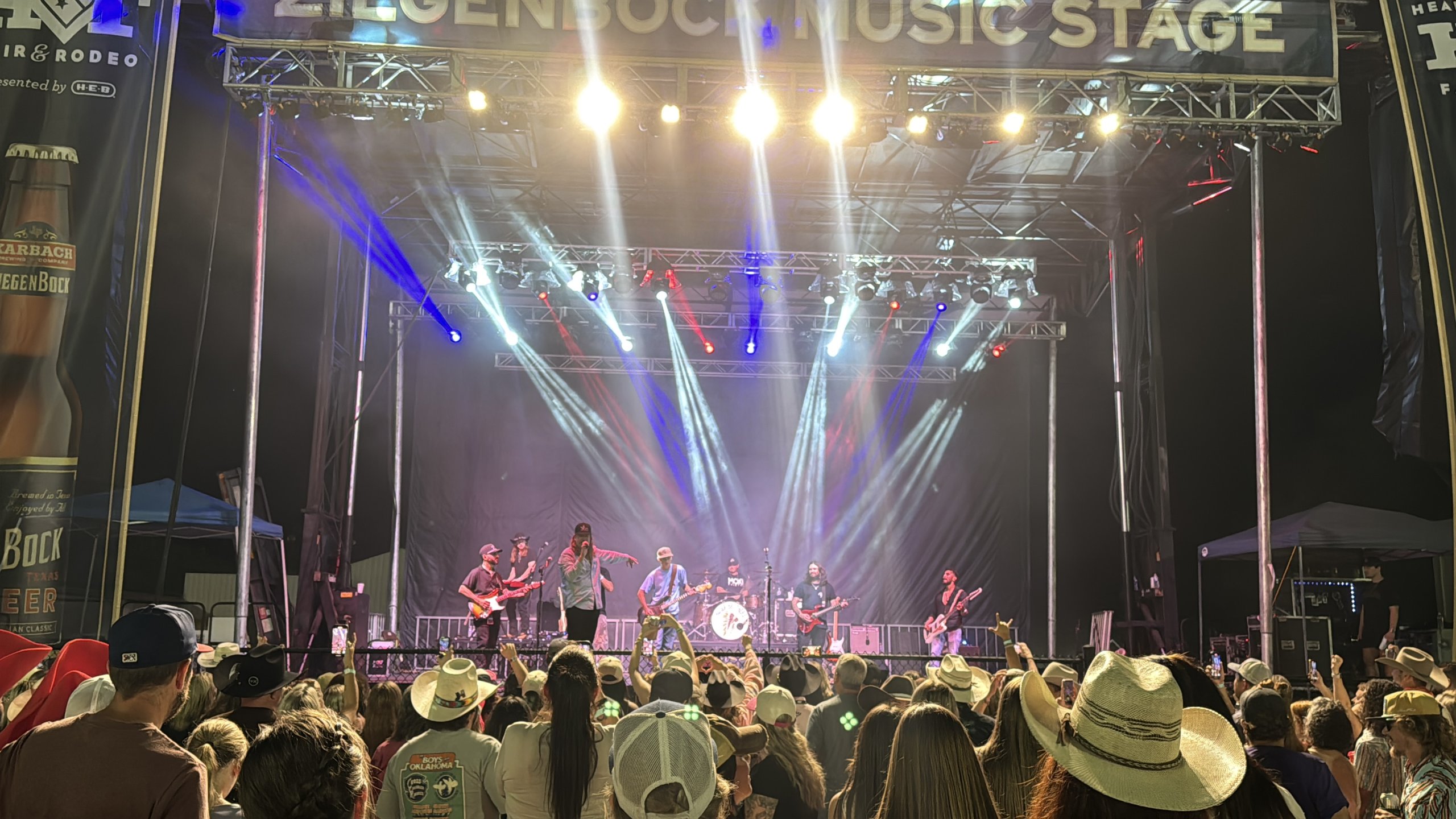 A band performs on a brightly lit outdoor music stage before a large crowd in McLennan County, Texas.