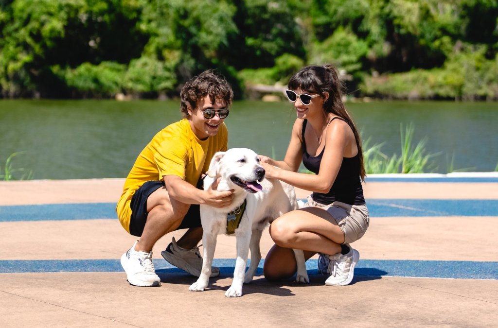 A young couple crouches down to pet a white dog by a river in McLennan County, Texas.