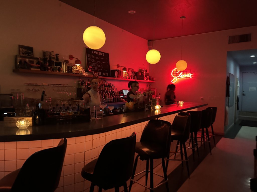 A dimly lit bar with red lighting, globe pendant lights, and bartenders behind the counter in McLennan County, Texas.