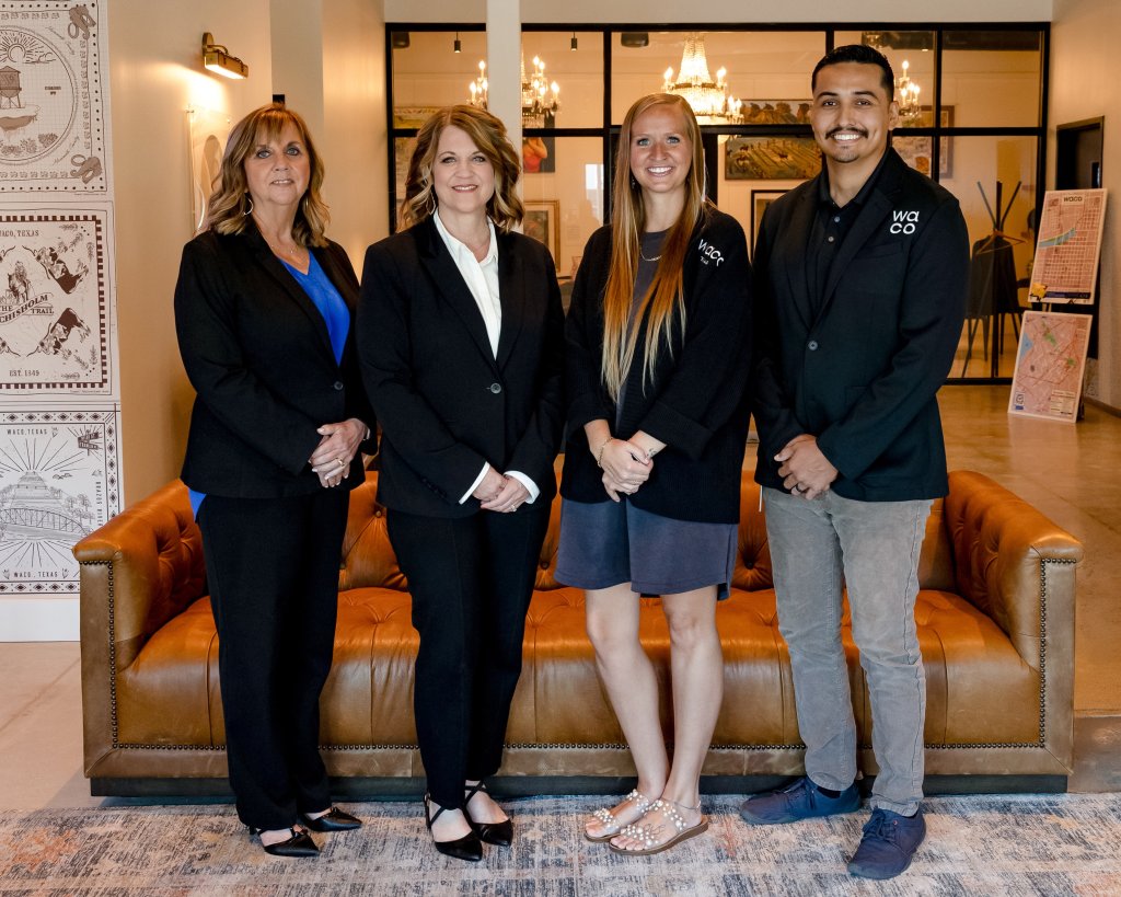 Four people stand in a row in front of a brown leather sofa in McLennan County, Texas.