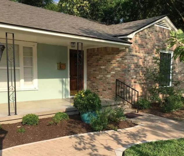 A single-story brick house with a light green porch and a paved walkway in McLennan County, Texas.