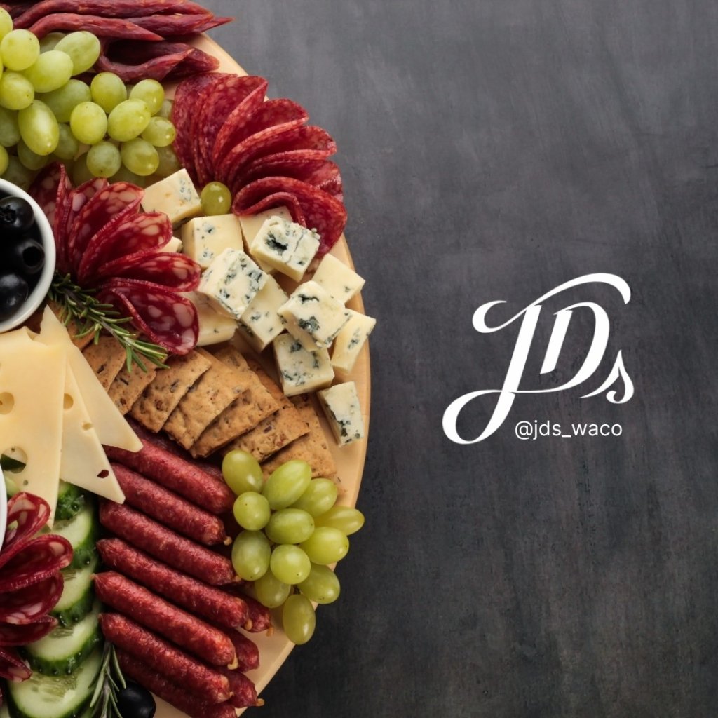 A charcuterie board featuring meats, cheeses, grapes, and crackers on a dark surface in McLennan County, Texas.