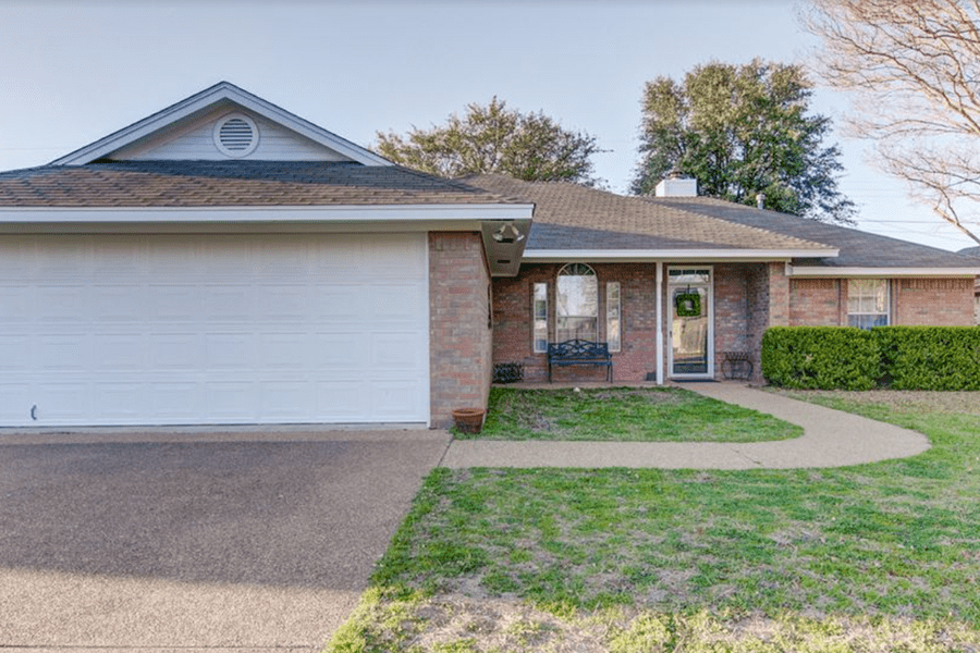 A single-story brick house with a large white garage door and a front walkway in McLennan County, Texas.