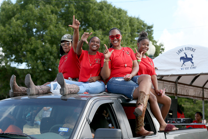 Four women in red shirts sitting on top of a truck during a parade in McLennan County, Texas.