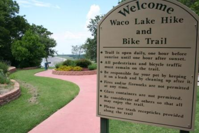 A sign for the Waco Lake Hike and Bike Trail stands near a path in McLennan County, Texas.