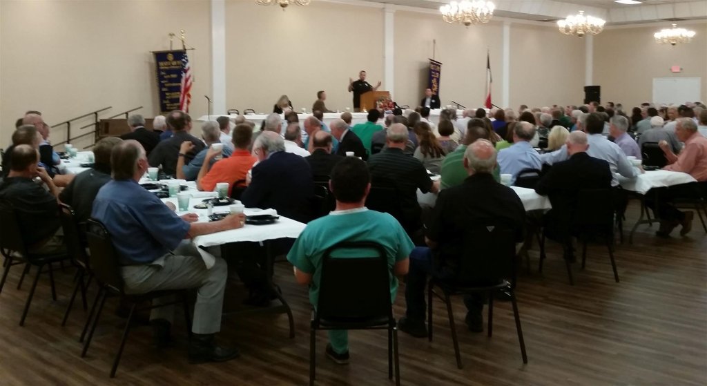 A speaker addresses a large audience seated at tables in a banquet hall in McLennan County, Texas.