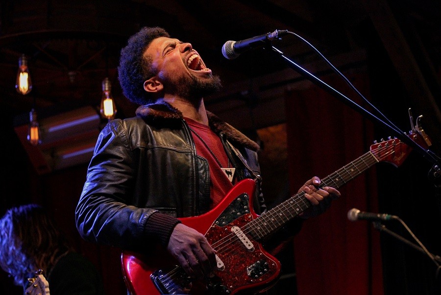 A passionate musician singing into a microphone while playing a red electric guitar in McLennan County, Texas.
