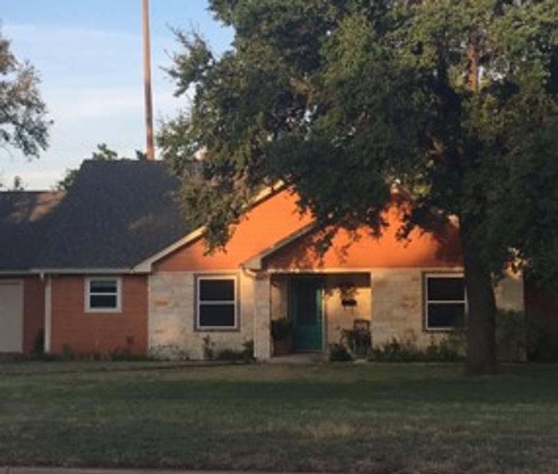 A single-story house with stone and orange siding under a large tree at sunset in McLennan County, Texas.