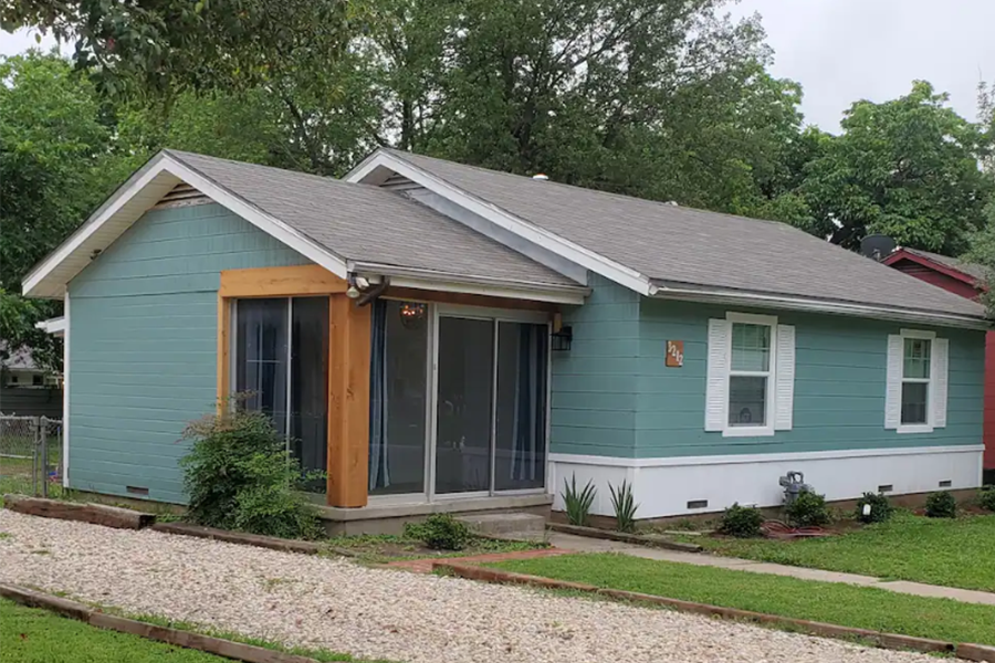 A single-story blue house with white trim and a gravel driveway in McLennan County, Texas.