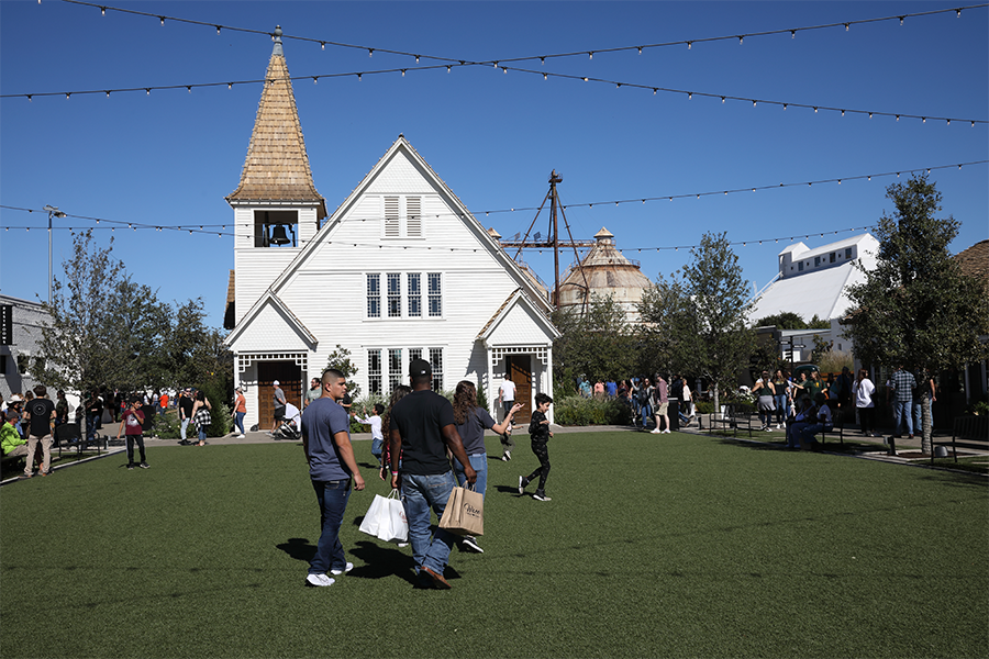 People walk across a green lawn in front of a white wooden church building in McLennan County, Texas.