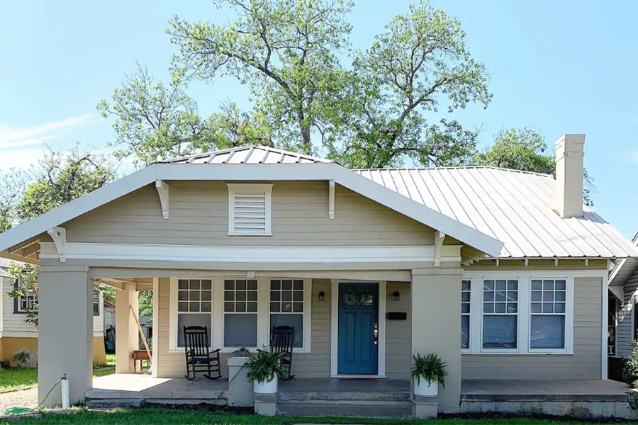 A tan bungalow house with a blue front door and a metal roof in McLennan County, Texas.